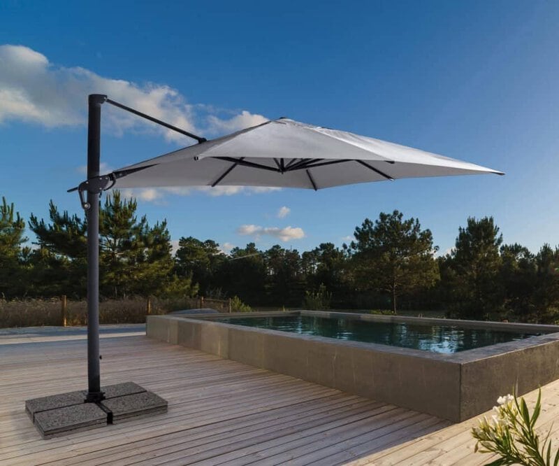 Ombrellone bianco sopra piscina all'aperto in un ambiente naturale con pini e cielo sereno.