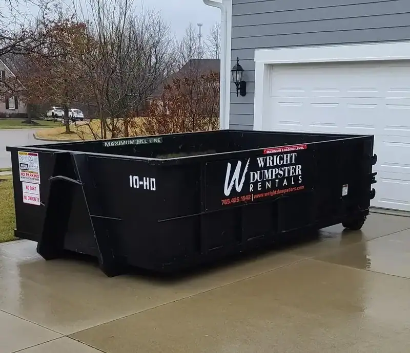 A black 10-HO dumpster from Wright Dumpster Rentals, placed on a concrete driveway in front of a house