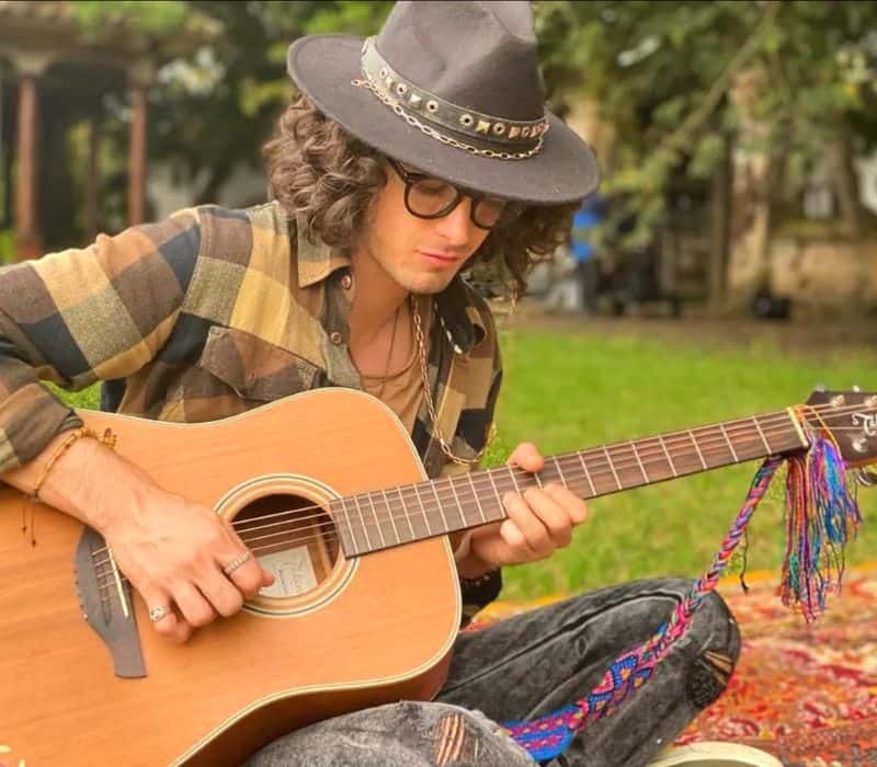 mexican actor Xabiani Ponce de Leon sitting in a park and playing the guitar