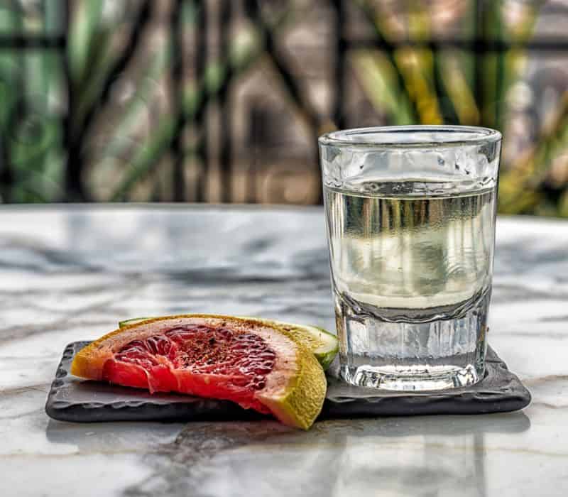 small cup of clear mezcal and orange slice