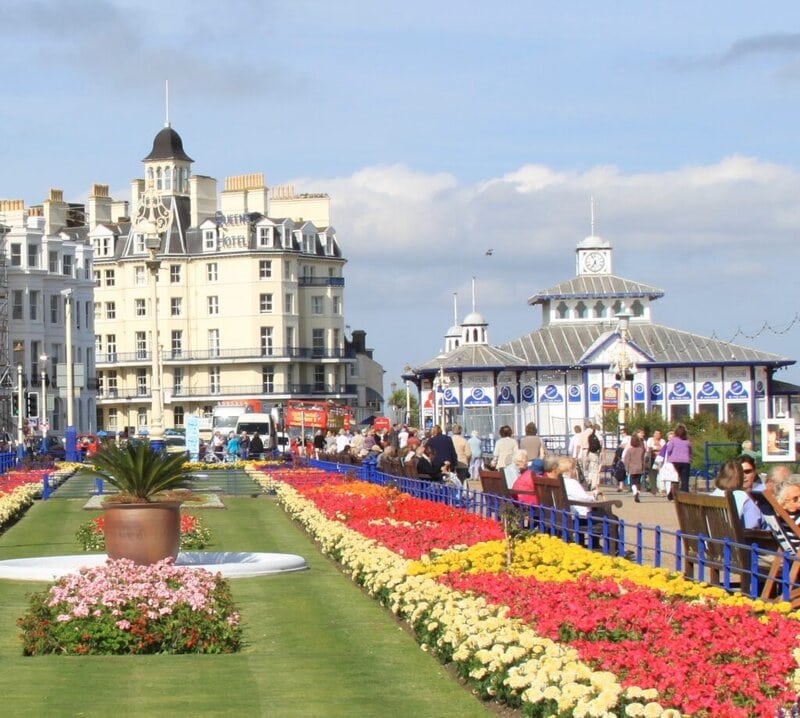 Blumenbeete, Promenade und historische Architektur an der Seafront von Eastbourne, mit Blick auf den Pier und das Queens Hotel.