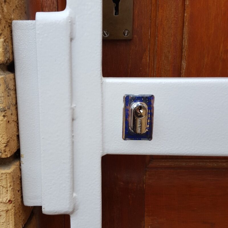 Heavy-duty locking cover plate with euro cylinder fitted to steel swing gate beside timber door panel.