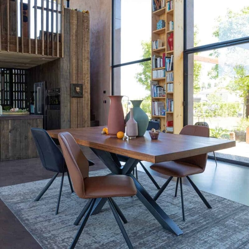 Ampia sala da pranzo moderna con tavolo in legno e sedie di design, grandi finestre e libreria alta, luminoso e accogliente.