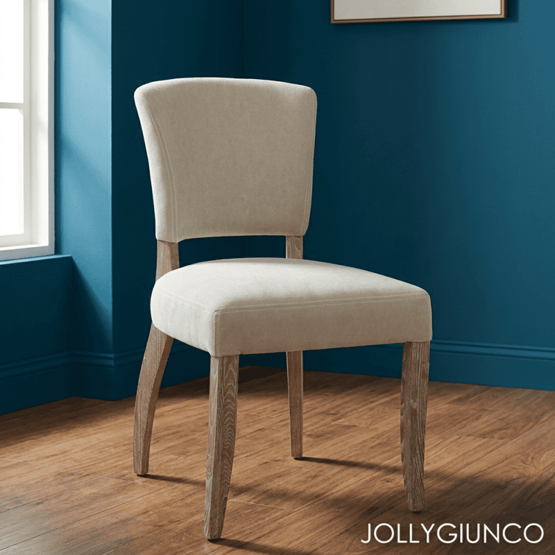 Beige upholstered dining chair with wooden legs on a blue-walled room by a window.