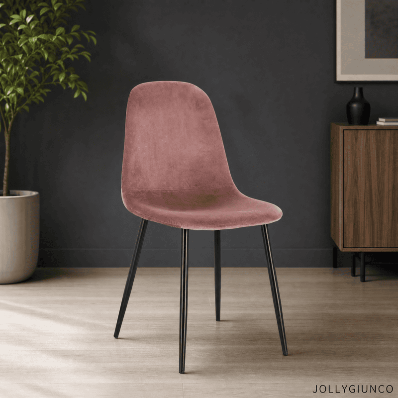 Pink velvet chair with black legs in a minimalist room, plant on the left and a wooden cabinet on the right against a dark wall.