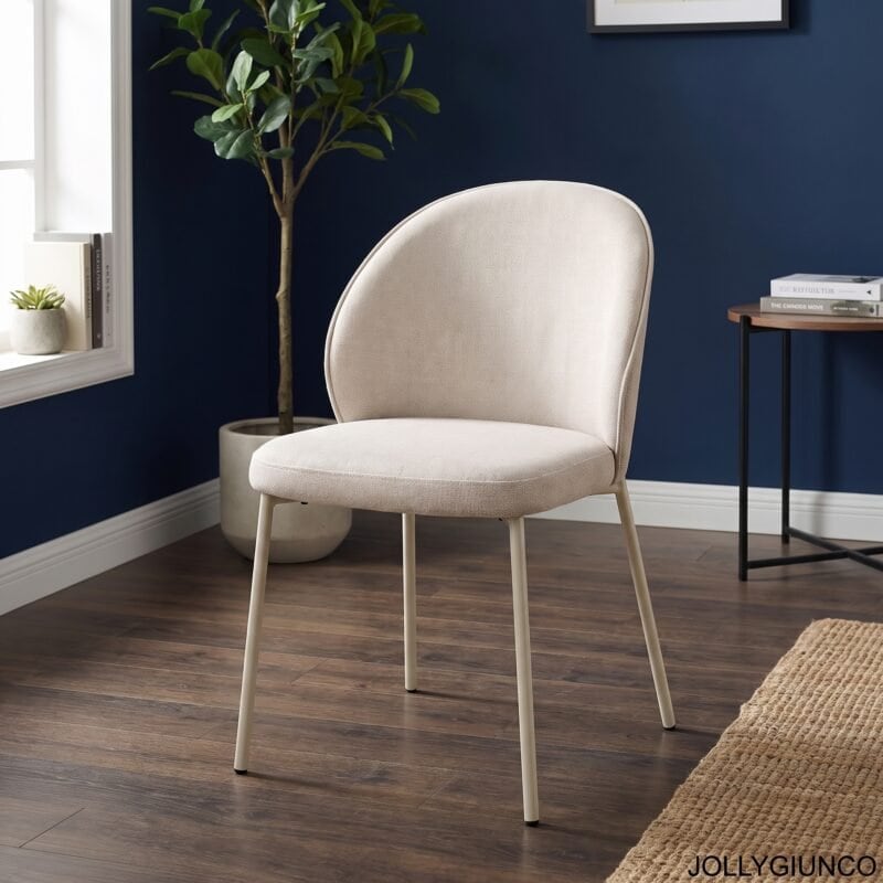 Beige upholstered chair in a navy blue room with a potted plant and stack of books on a small table nearby.