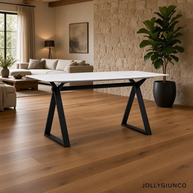 Modern white rectangular table with black angled legs in a cozy living room, beige sofa, wood floors, and a tall potted plant in the background.