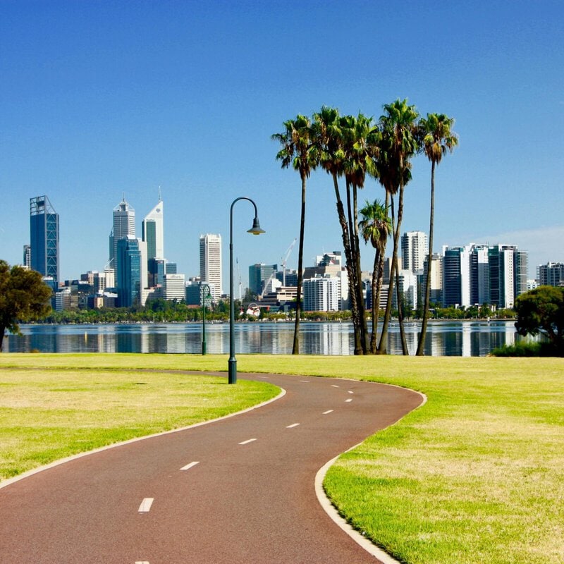 Panorama von Perth mit Skyline, Radweg und Palmen am Flussufer.