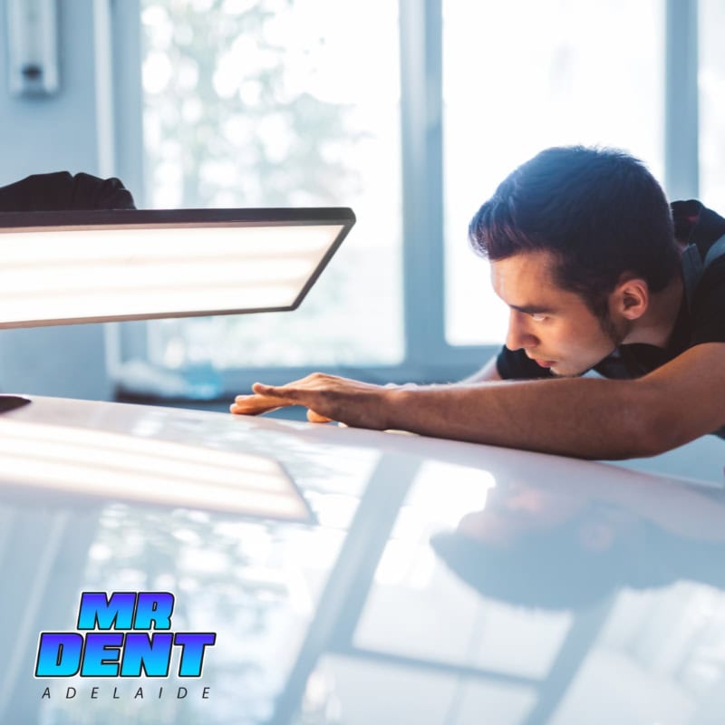 Close-up of a man inspecting a car's surface under bright light while performing paintless dent removal in West Lakes to eliminate dents without damaging the paint.