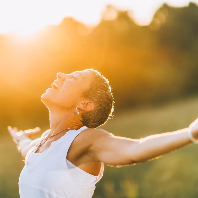 Dona radiant amb els braços oberts gaudint del sol i la natura