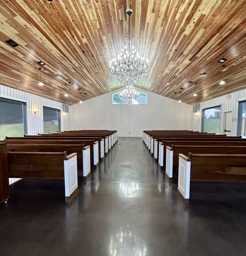 Interior of the wedding chapel with wooden pews, chandelier and stained glass at Romaine Valley Weddings & Events in Fenton, Missouri