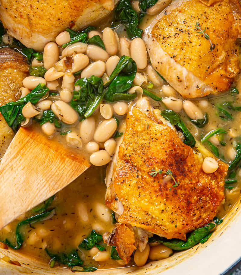 close up of saucy white beans and spinach cooked with chicken thighs