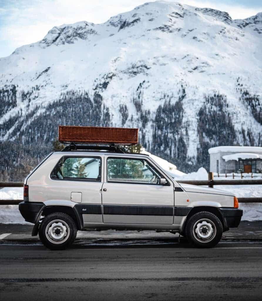 Auto d'epoca in montagna innevata con sfondo di cime alpine.