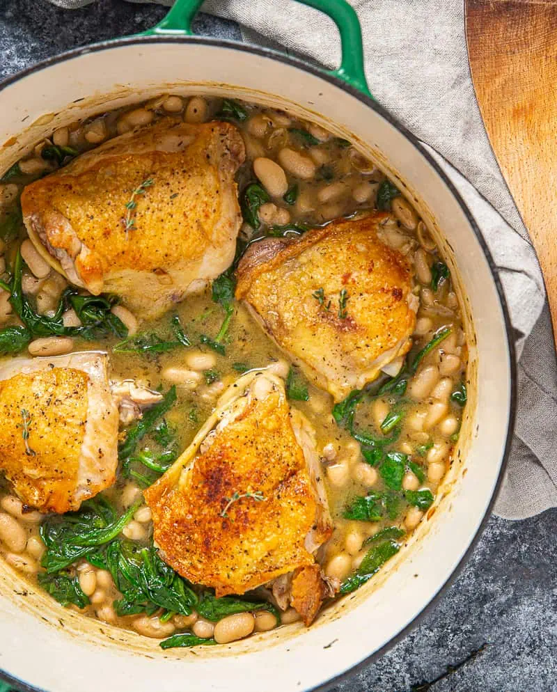 chicken thighs in dutch oven with saucy white beans and spinach