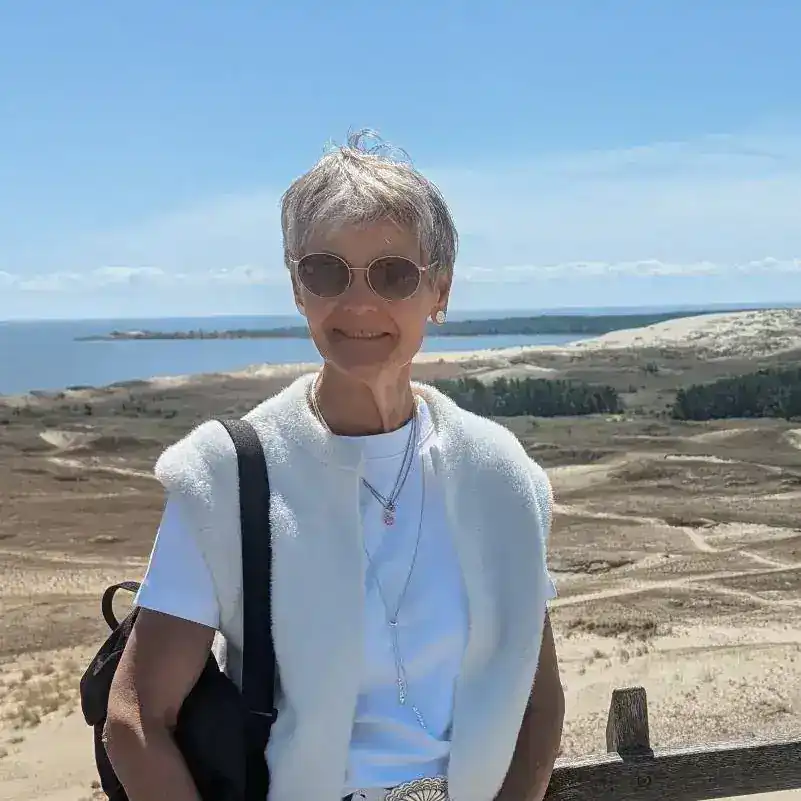 Ältere Frau mit Sonnenbrille und Rucksack am Strand.