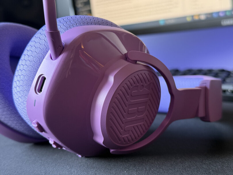 Close-up of JBL Quantum 360 purple over-ear headphone with a textured design on a blurred background.