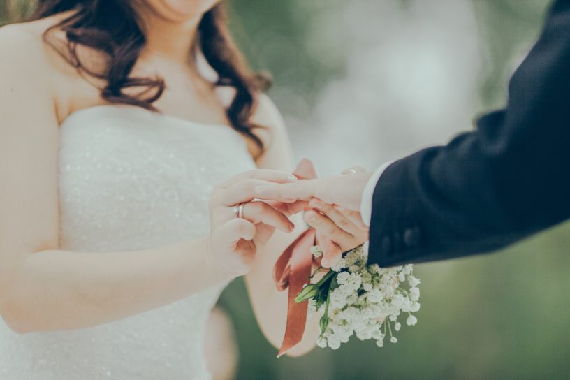 Frau trägt Brautkleid und hält die Hand ihres Ehemanns.