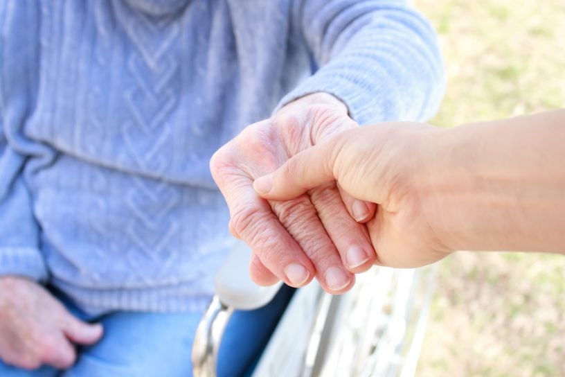 Eine Person im Rollstuhl greift eine andere Hand
