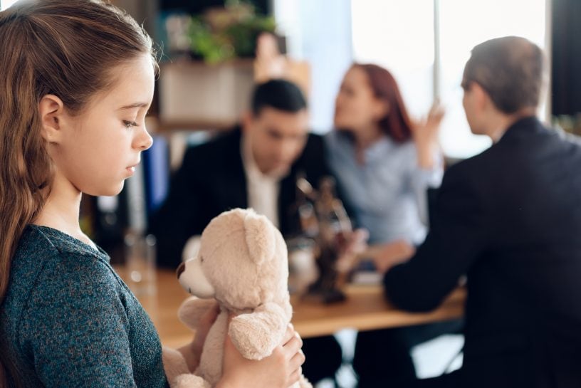 Eltern reden mit dem Anwalt und das Kind guckt auf ihren Teddy.