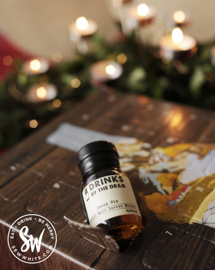 A small bottle in the whisky advent calendar with greenery and candles in the background