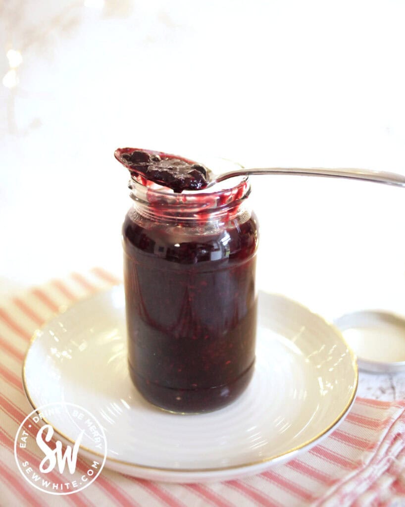 a red jar of mixed berry compote with a spoon balanced on top