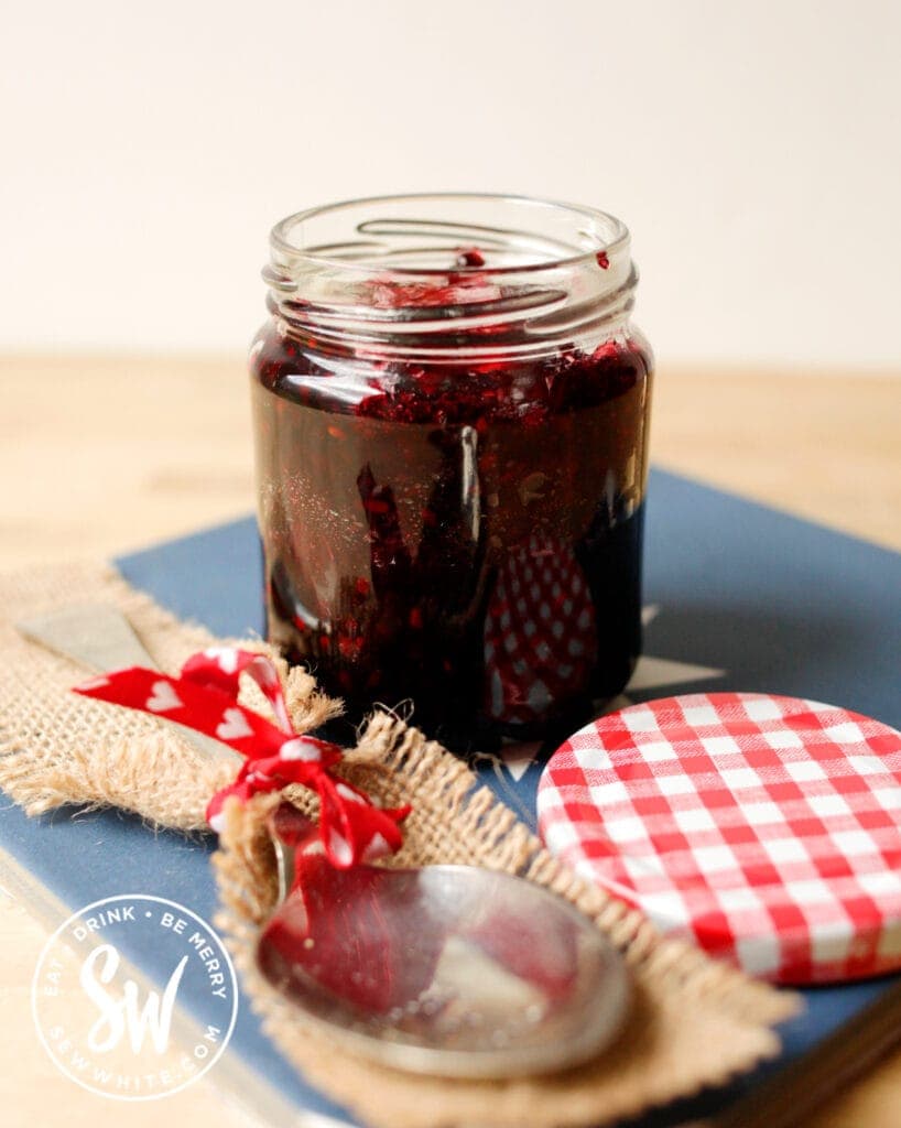 blackberry jam in a jar with jam spoon and lid on a blue tile