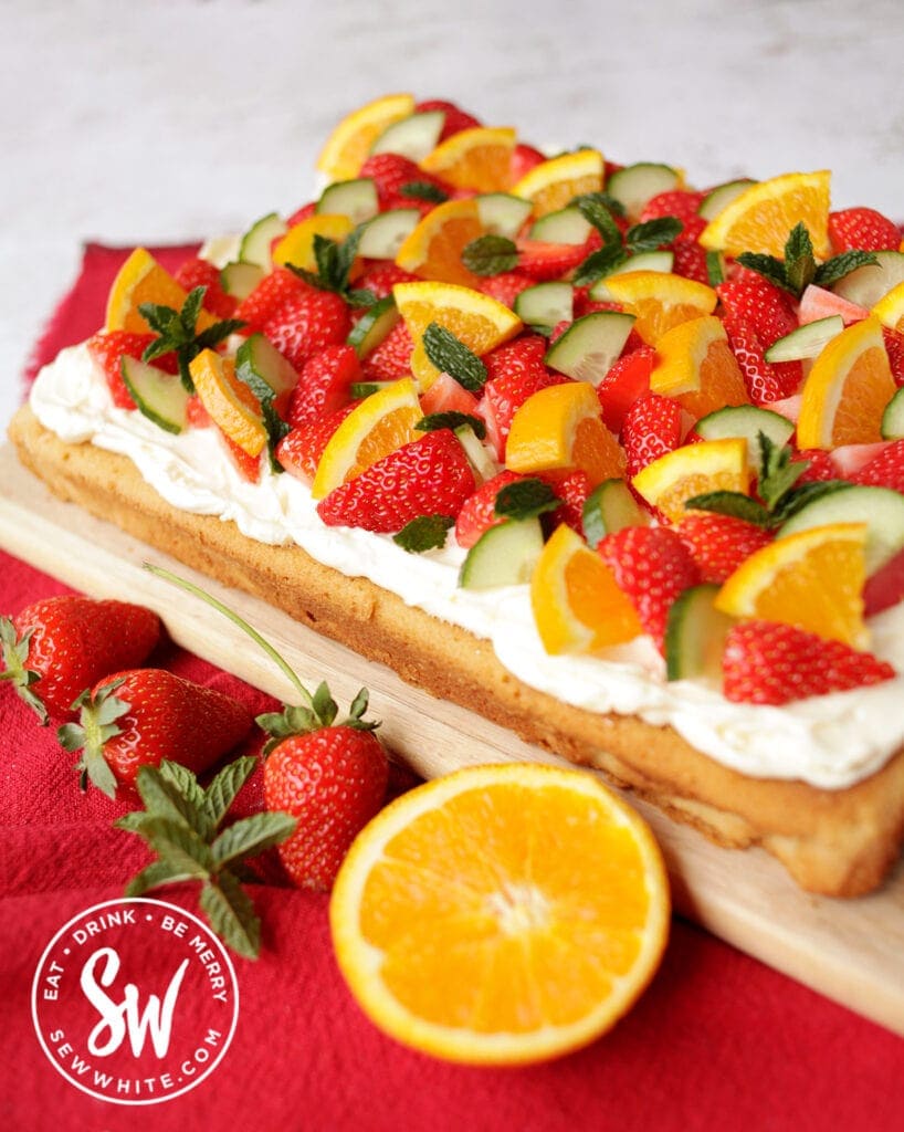 The finished pimms traybake covered with pimm's fruit of strawberries, oranges and cucumber with fresh mint