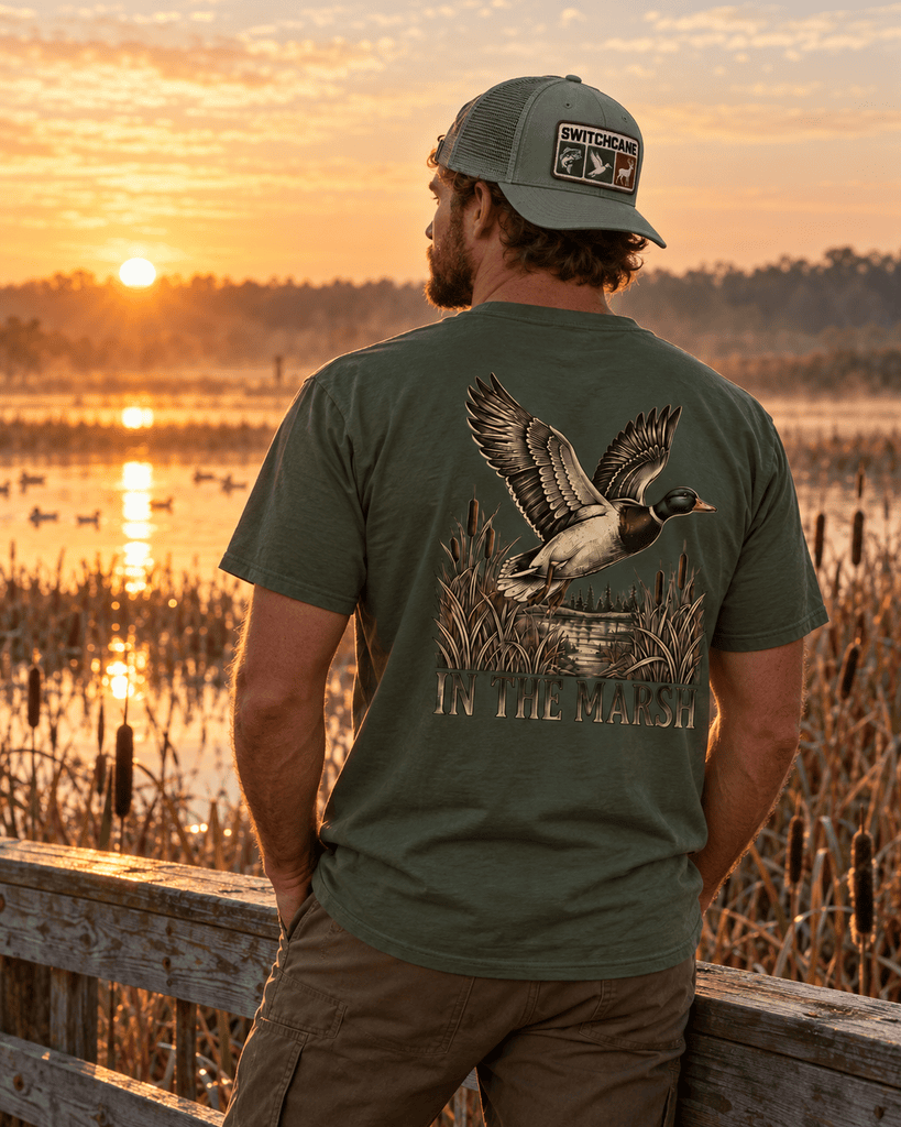 A man in the In the Marsh Shirt looking at the lake