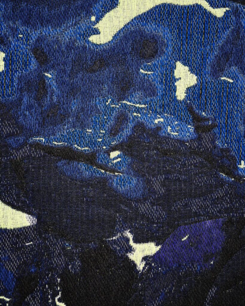 Abstract image of dark blue and black textured fabric with lighter patches, resembling denim material. The pattern appears random, with some white highlights scattered across the surface.