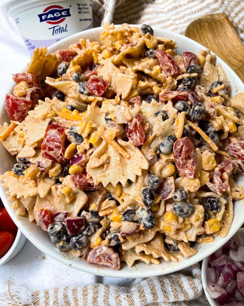 southwestern taco pasta salad in white serving bowl next to wooden spoon and greek yogurt