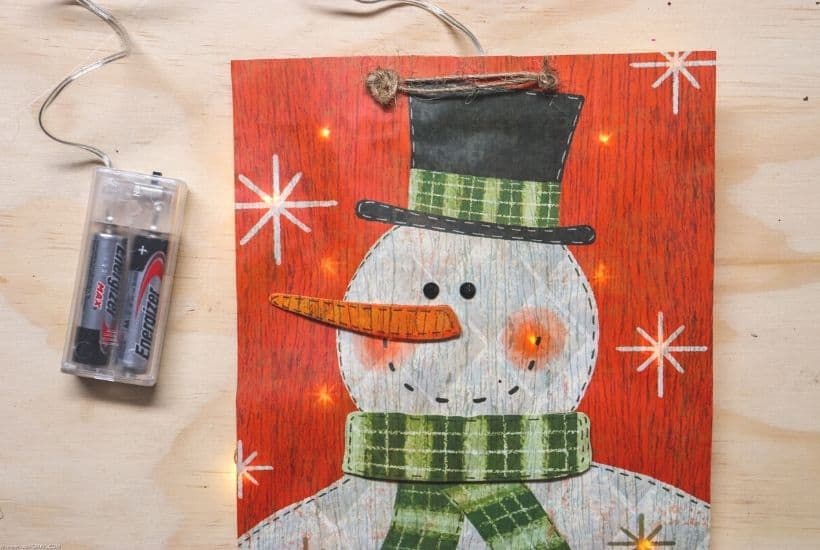 Decorate your home for the holiday season with this easy-to-make Lighted Snowman Picture. It’s fun to put together and perfect for hanging up around the home to get into the holiday spirit. This DIY Christmas craft is made with a gift bag and a dollar store frame. It is a fun dollar store Christmas craft.