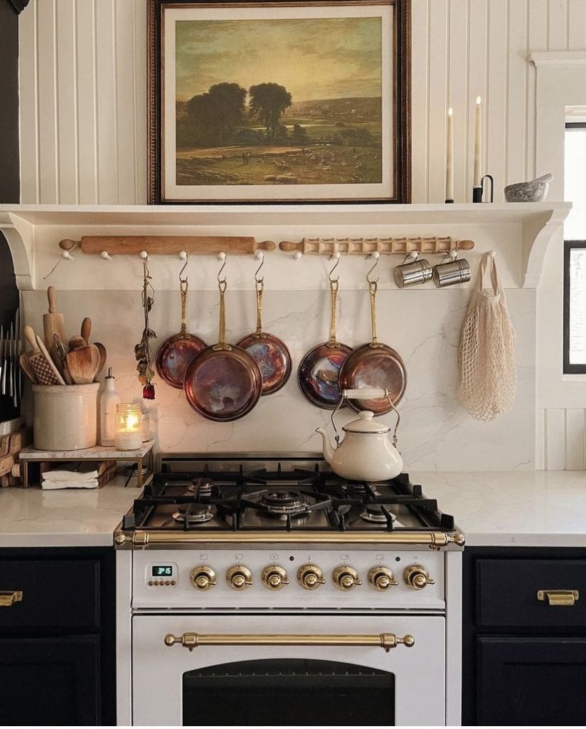 Elegant kitchen with black cabinets, white counters, and white stove styled with copper pots, a white tea kettle, and wooden spoons in a white vase — sophisticated top of stove decor ideas from By Paige Nicole.