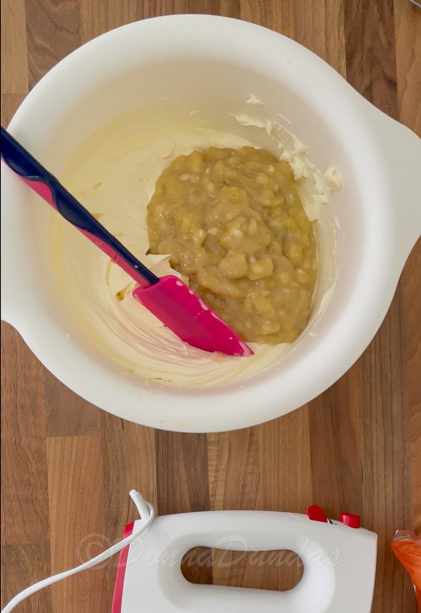 mashed banana piled on cream in mixing bowl.