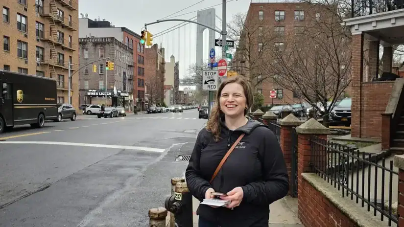 Kayla Santosuosso standing with campaign literature on 3rd Avenue in Bay Ridge, Brooklyn with the Verrazzano Narrows Bridge in the background.