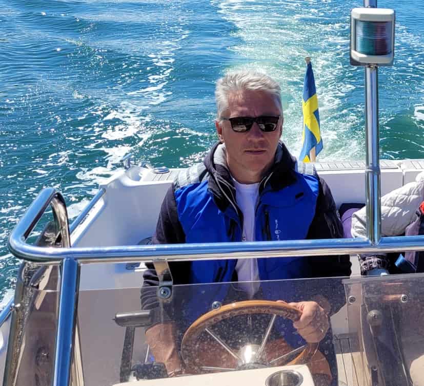 Fartygskapten på båt med svensk flagga, havsutsikt och vatten, som representerar trygghet, certifierad sjöfart och maritim säkerhet.