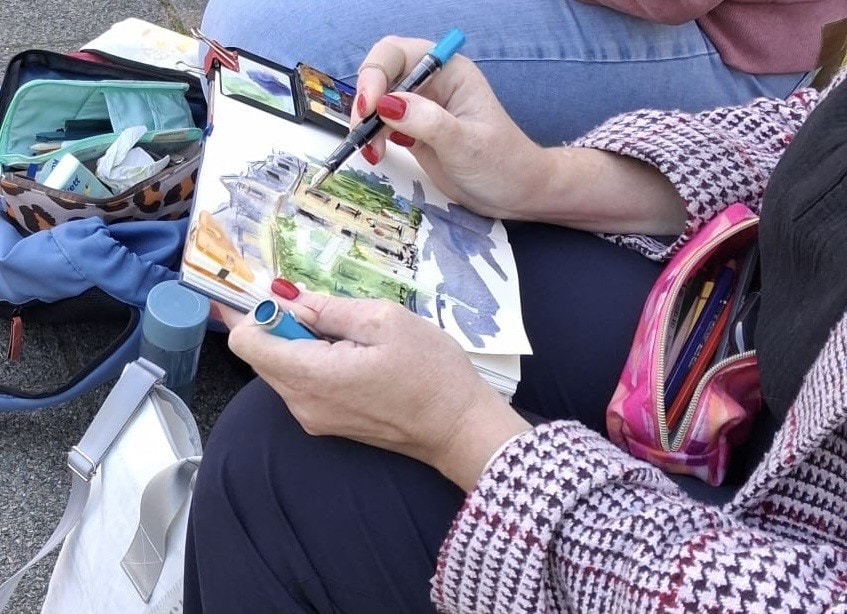 Nahaufnahme eines Skizzenbuchs während einer Urban-Sketching-Session. Zu sehen sind Aquarellfarben, Stifte und eine teilweise fertiggestellte Architekturzeichnung.