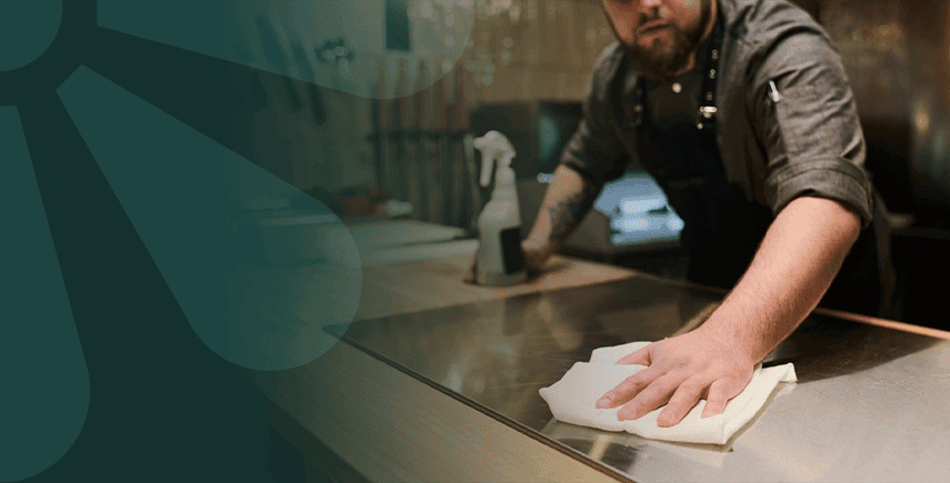 Chef wiping a kitchen counter with a cloth, ensuring odor control in a commercial kitchen setting.