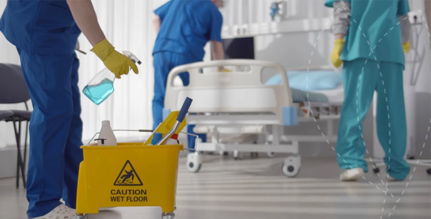 Staff cleaning a compact hospital ward with a caution wet floor sign, ensuring infection control.