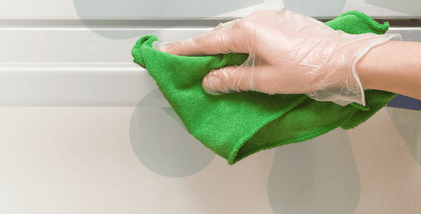 Hand in glove wiping a surface with a green cloth, demonstrating hygiene practices for a clean environment.