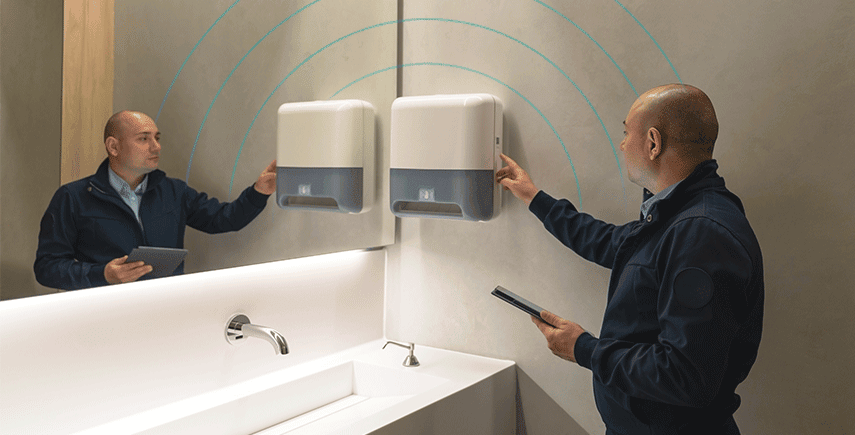 Staff conducting a hygiene audit in a washroom, checking paper towel dispensers with a tablet.
