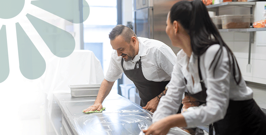 Chefs cleaning a mega kitchen counter with a green cloth, ensuring a spotless and hygienic workspace.