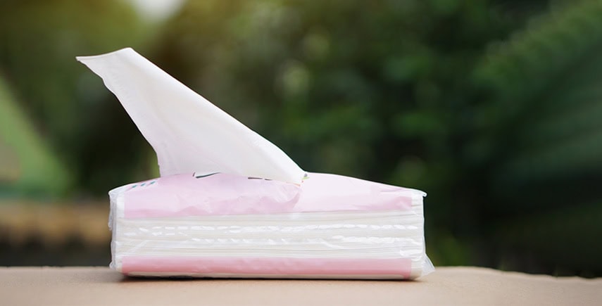 Pink tissue box with a tissue pulled out, placed on a table for personal hygiene use.
