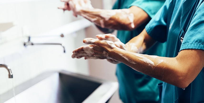 Healthcare workers washing hands at a sink, practicing moments of hand hygiene for infection prevention.