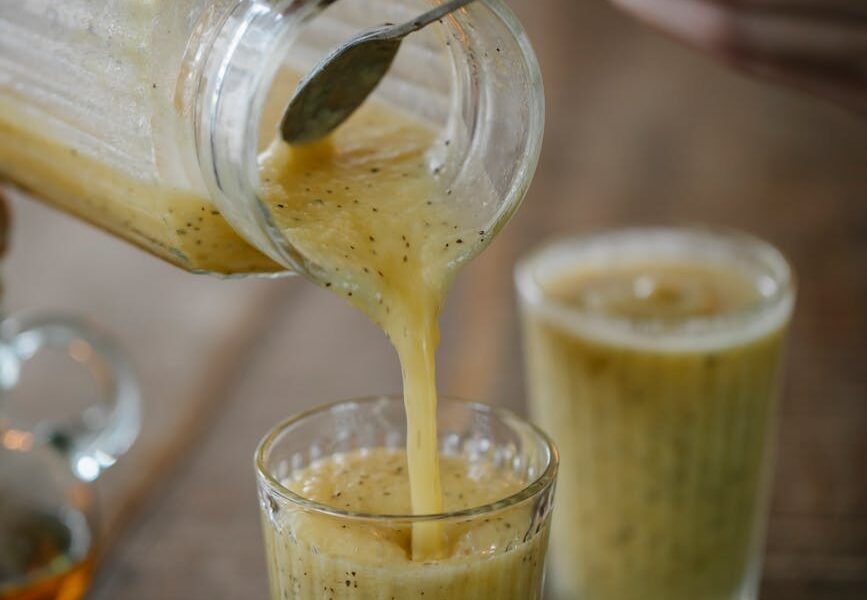 person pouring smoothie into a drinking glass