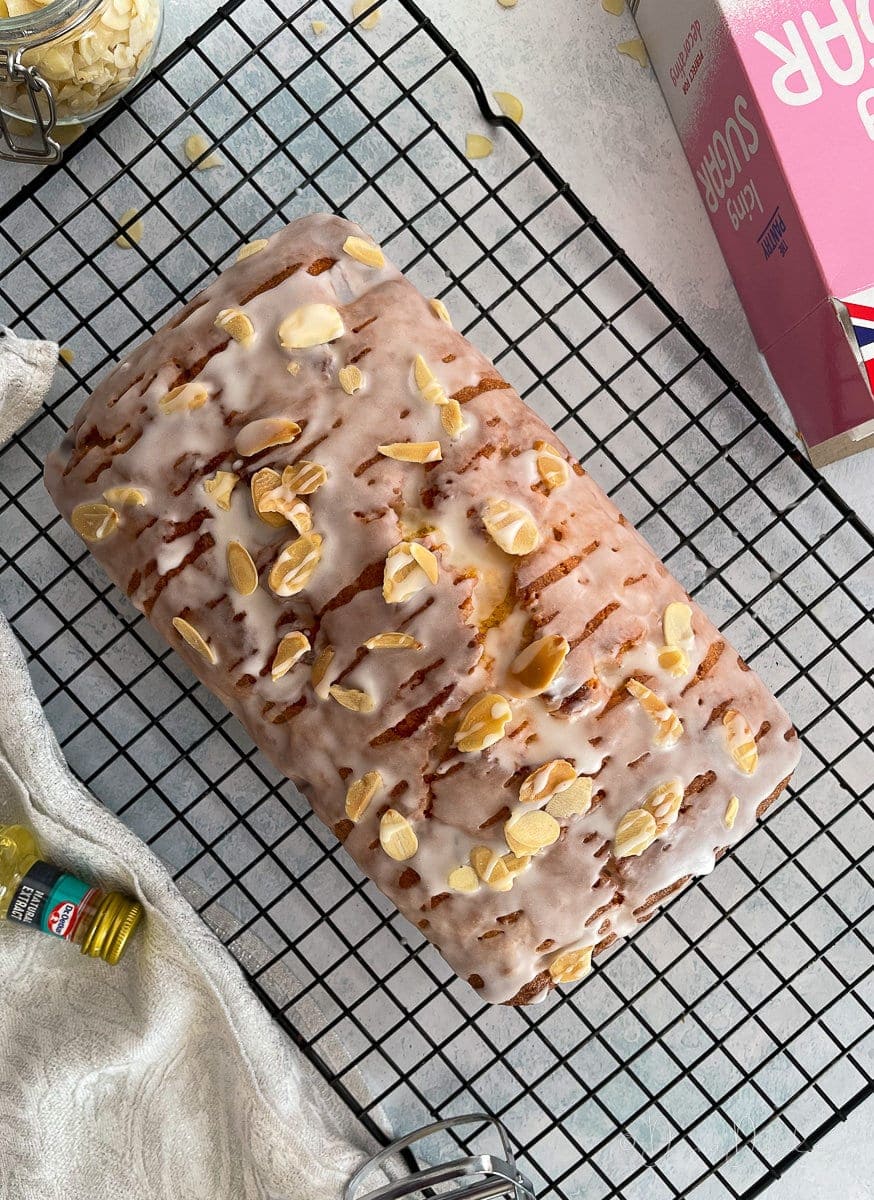 loaf cake topped with icing and almonds on wire rack.