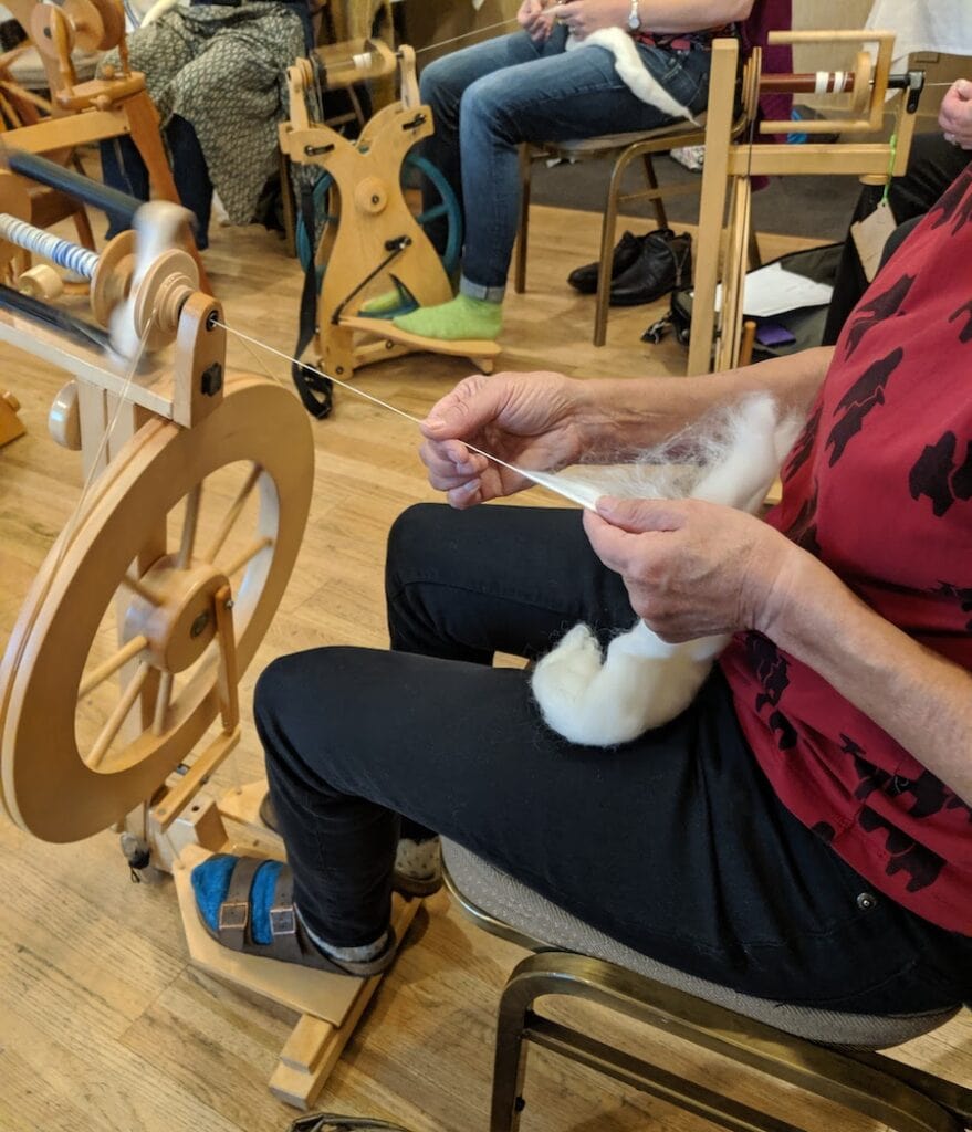 person in red shirt spinning white fiber with spinning wheel