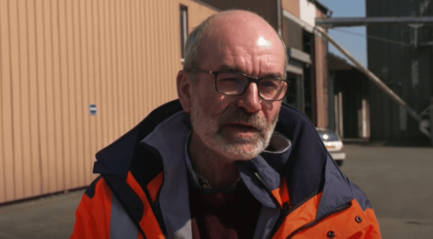 Homme en veste orange devant un silo agricole