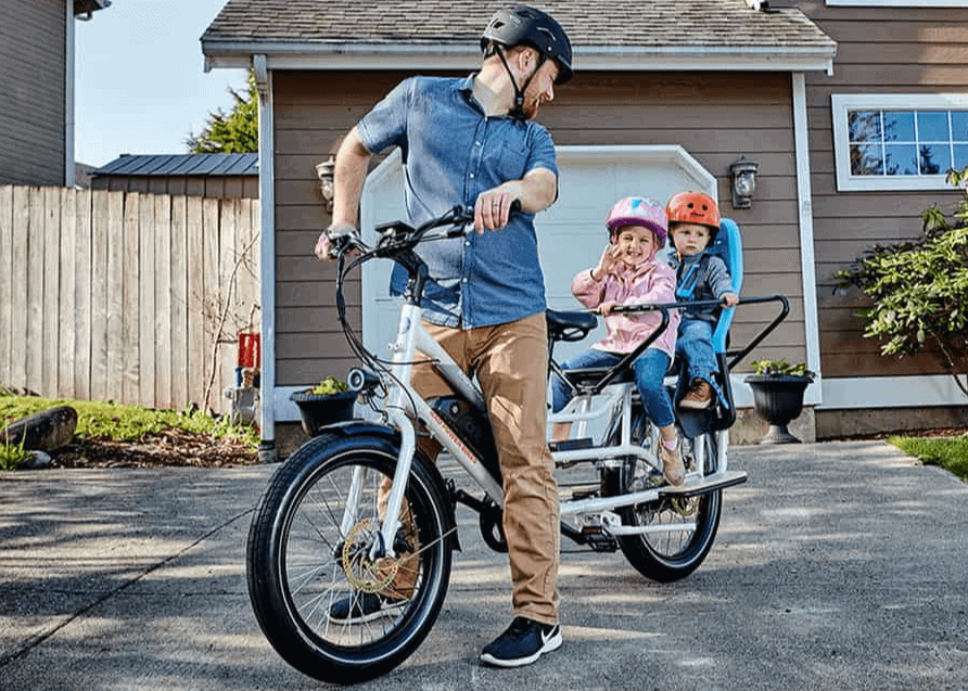 Father with two children on a compact family e-bike in front of a house.