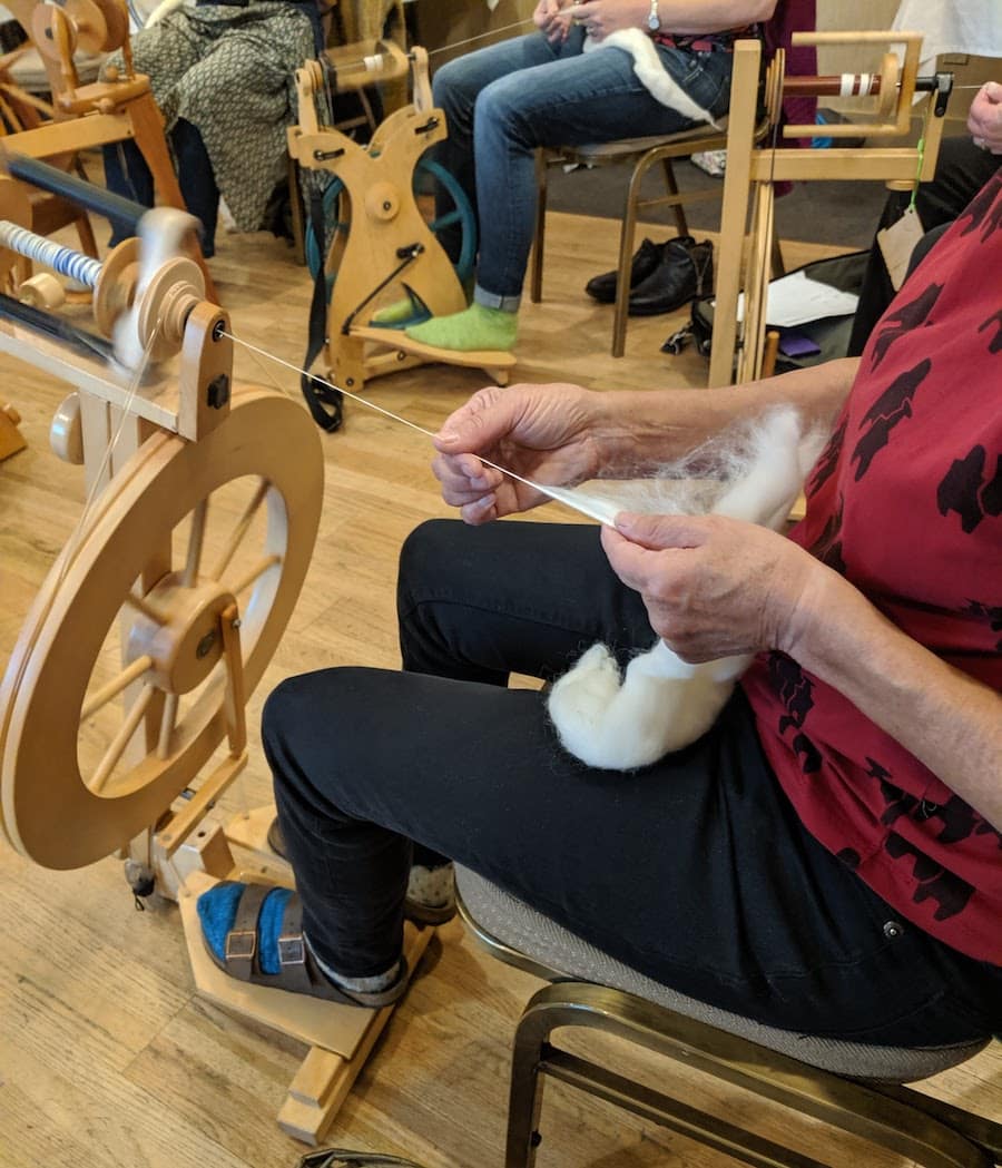 person in red shirt spinning white fiber with spinning wheel