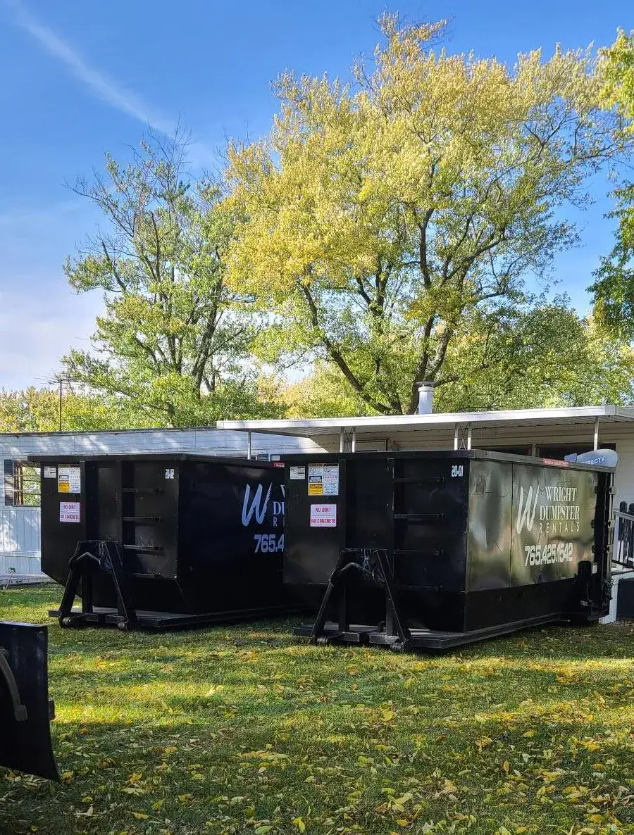 Two black dumpster with trees in the back